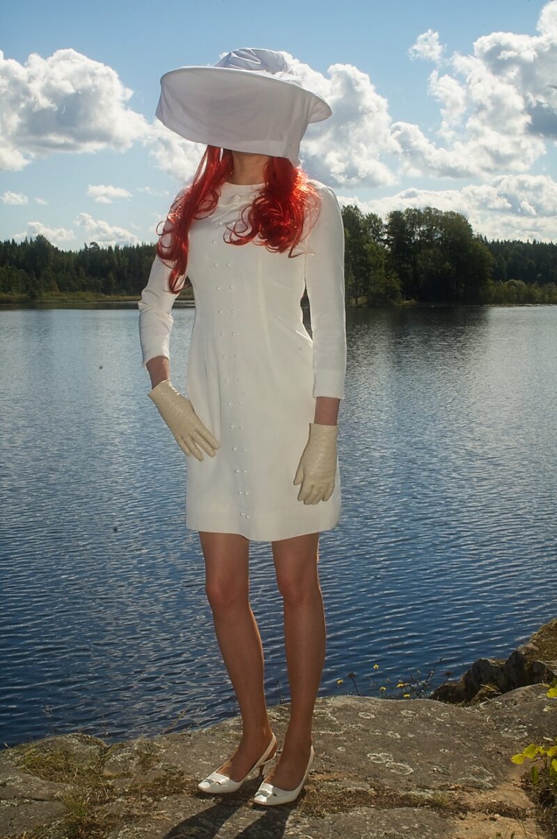 Der Tag am See. Im Vordergrund ein Fotomodell im Hintergrund ein See. Das Modell trägt ein weißes Kleid und helle Strümpfe.