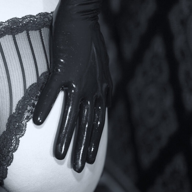 Glänzende schwarze 0,2 mm Latexhandschuhe. Die Hand liegt auf dem Po