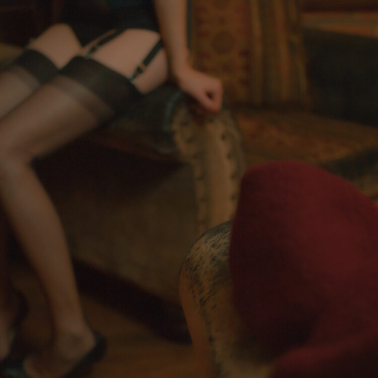 Straps & Strumpf. Ein sitzendes Fotomodell Lilly, das von der Seite fotografiert wurde