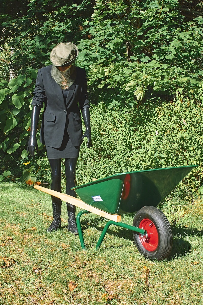 Ein Modell in 0,2 mm Latexstrümpfen und langen 0,2mm Latexhandschuhe. Im Vordergrund ist eine Schubkarre zu sehen