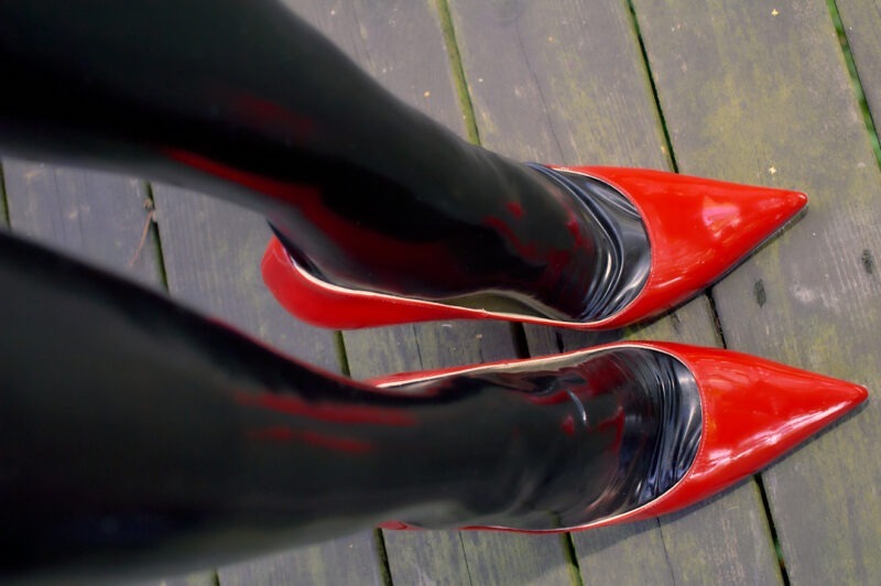Black AG Nahtstrumpf latex stockinged legs and feets and red Jimmy Choo High Heels. The Heels standing on a wooden floor