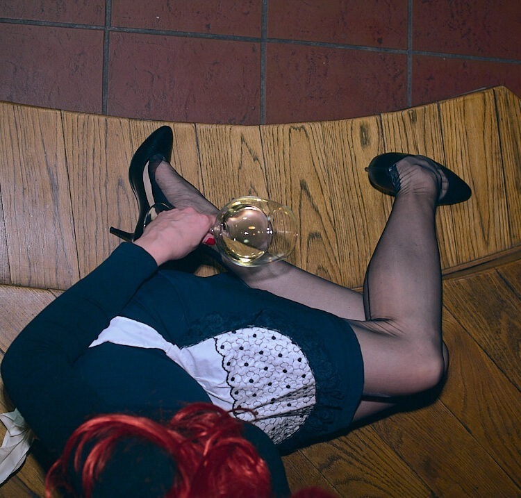 Women wearing a black and white maid outfit, black ff seamed nylons, and black shoes, holding a glass, sitting on wooden stairs
