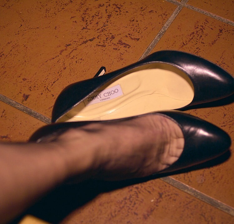 Bestrumpfter Fuß und zwei schwarze Jimmy Choo High Heels