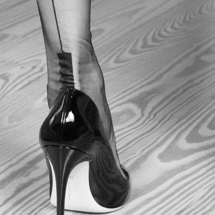 Detailaufnahme eines bestrumpften Frauenbeins. Das Model trägt echte Nahtnylons mit einer Cuban Heel- einer kantigen Hochferse. Sie trägt dazu schwarze High Heels